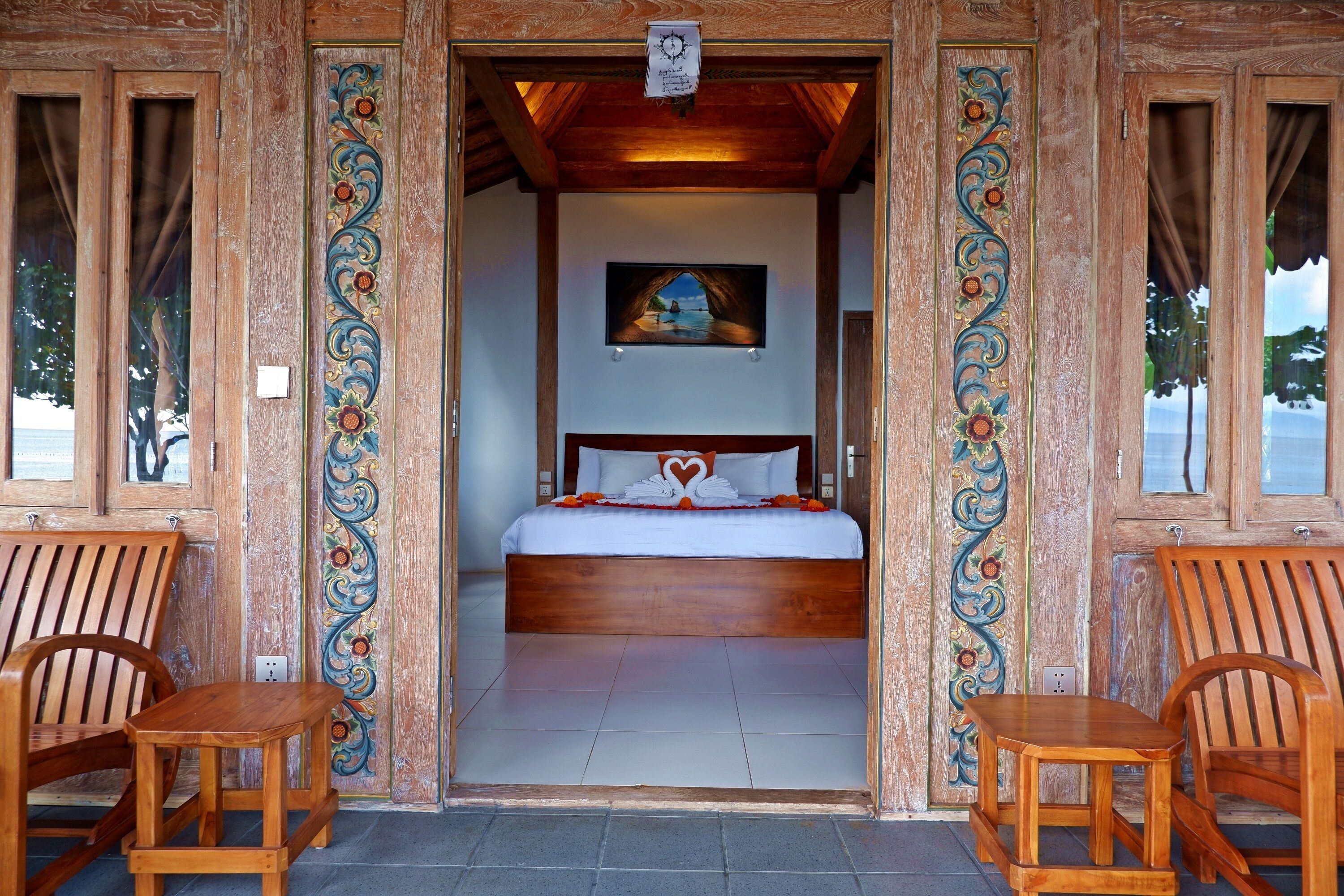 Een kamer met houten frame, een bed, twee stoelen en een schilderij aan de muur.