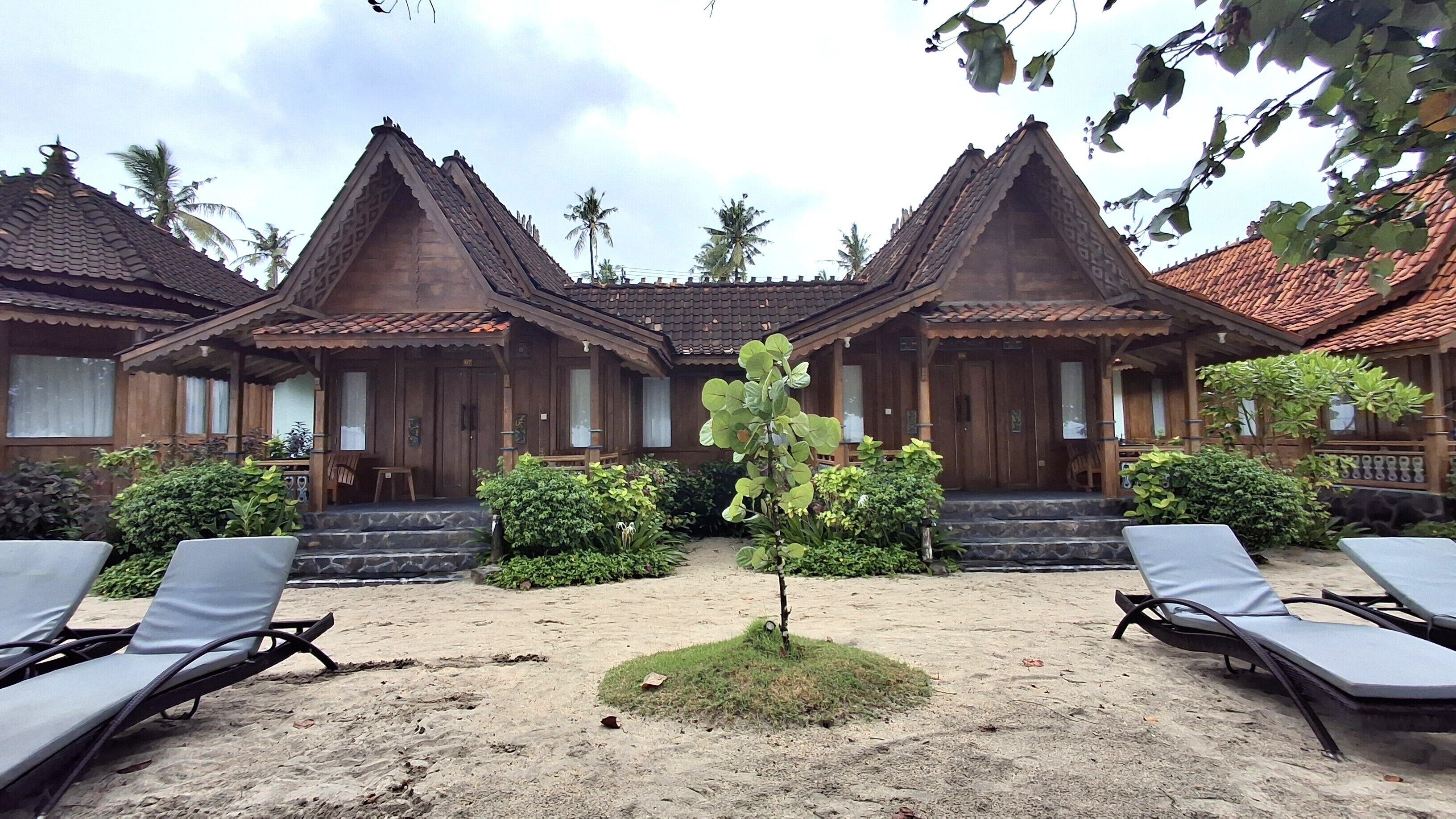 A traditional wooden building with a tiled roof, surrounded by a sandy area with lounge chairs.