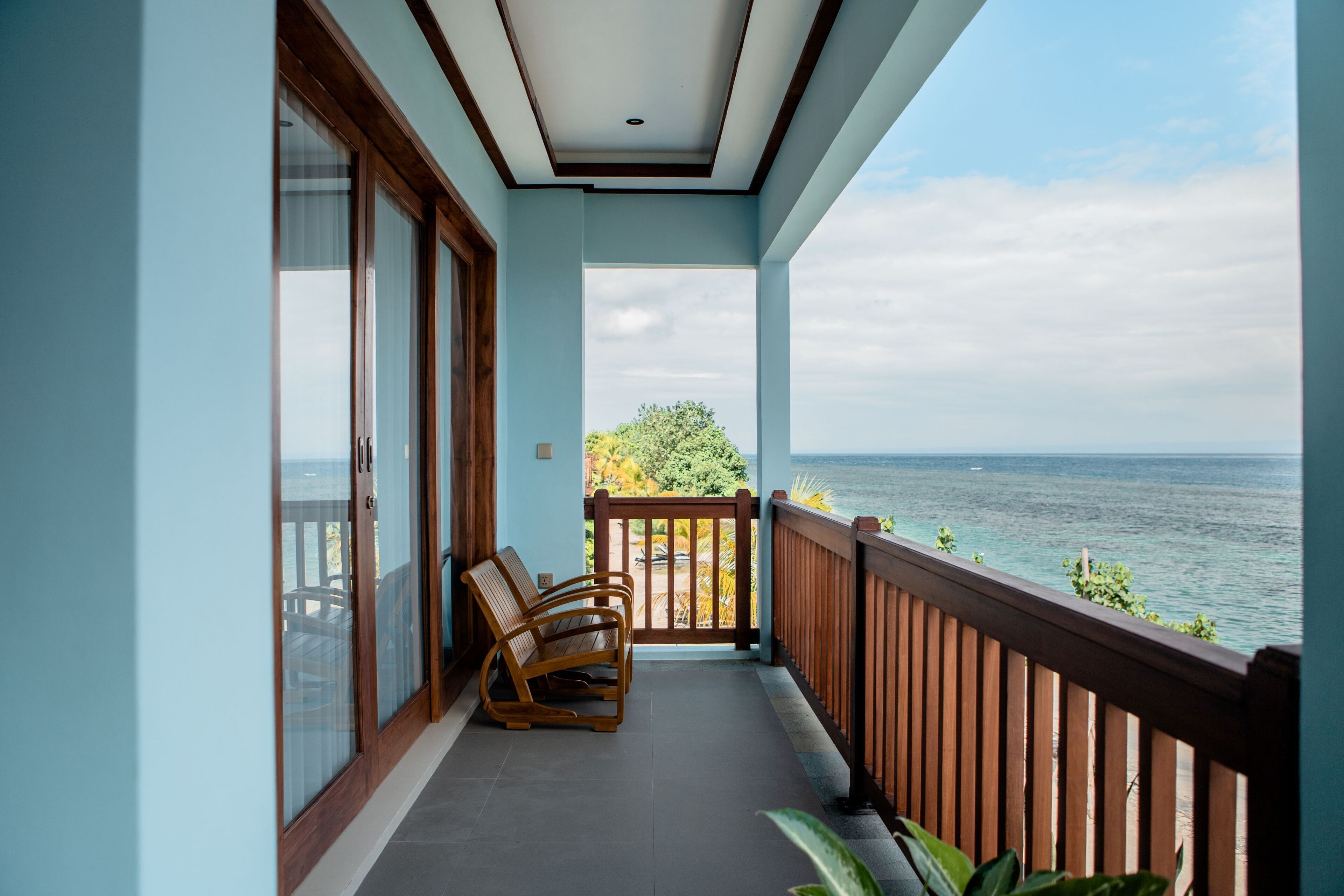 A balcony with a view of the sea, wooden chairs, and a plant.