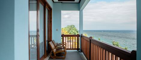 A balcony with a view of the sea, wooden chairs, and a plant.