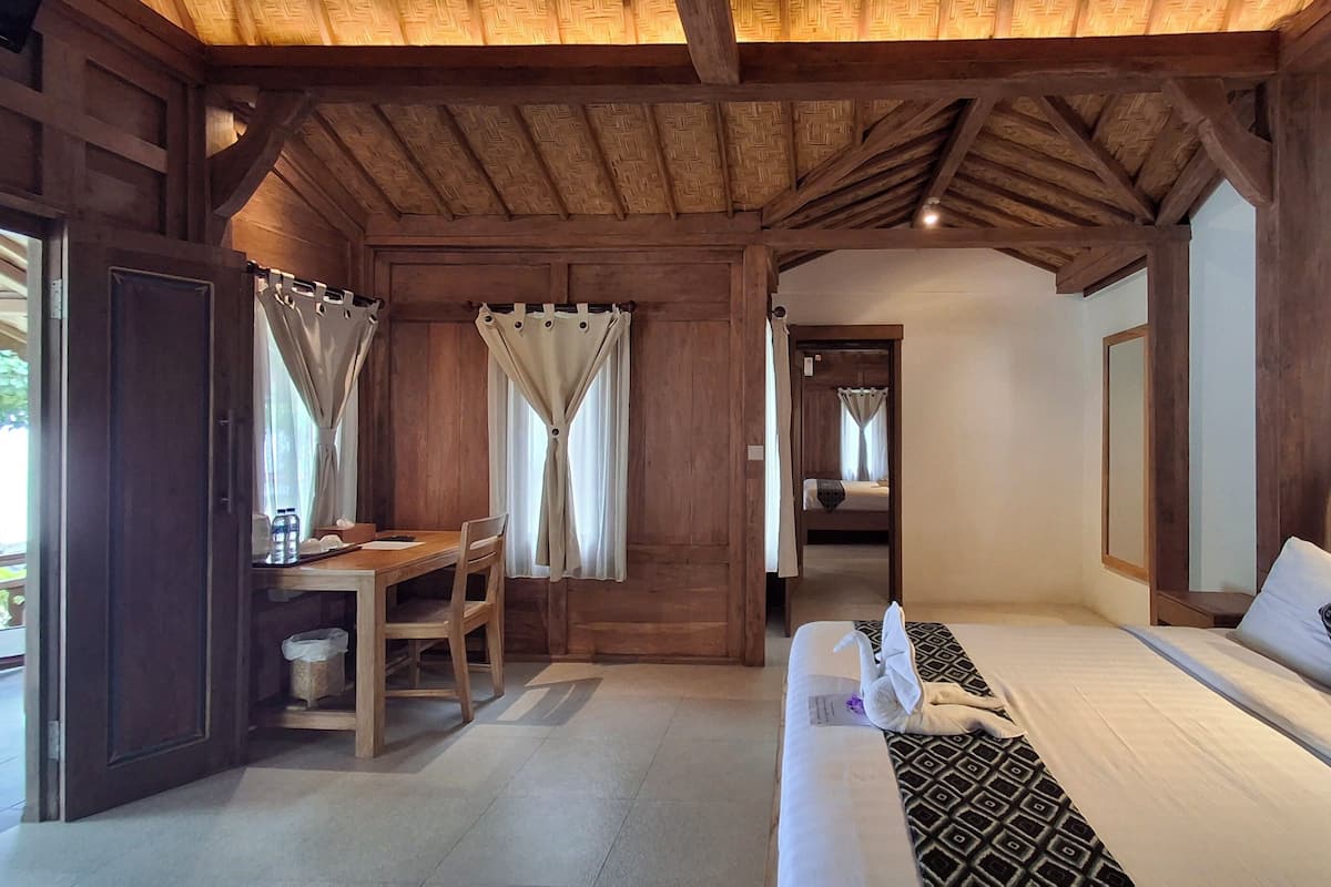 A room with a wooden ceiling, a bed with patterned pillows, a bedside table, and a desk with a chair.