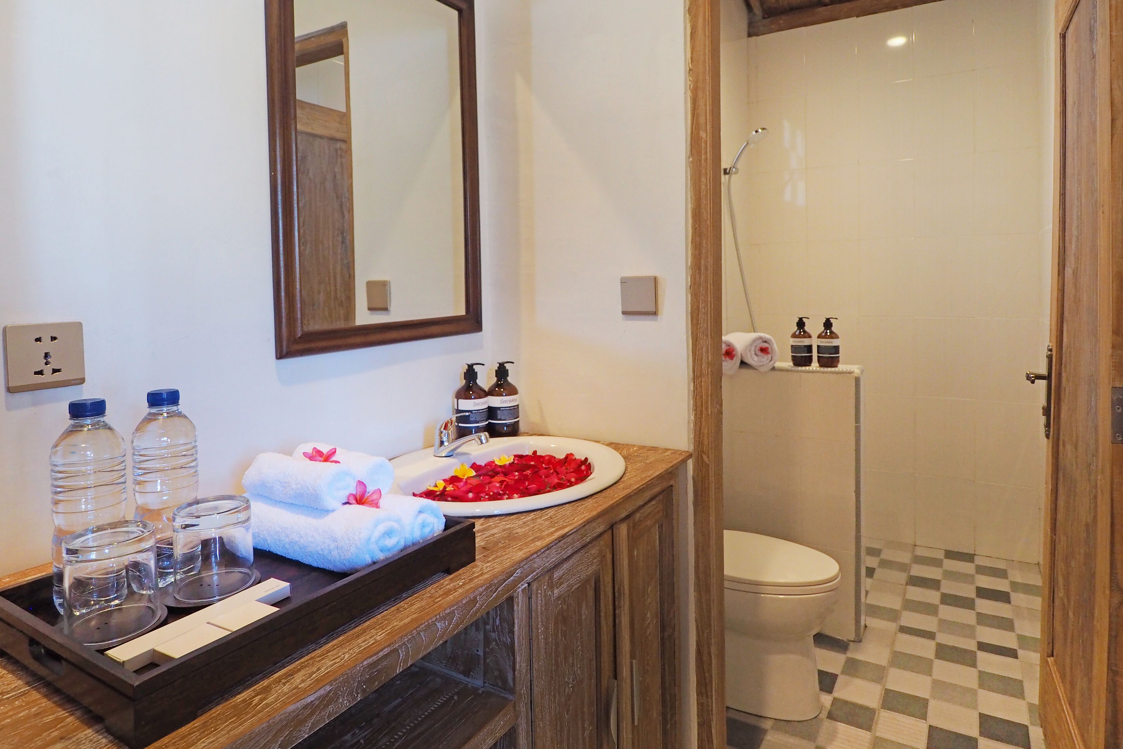 Une salle de bain avec un meuble-lavabo en bois, un évier, un miroir, une douche et des toilettes.