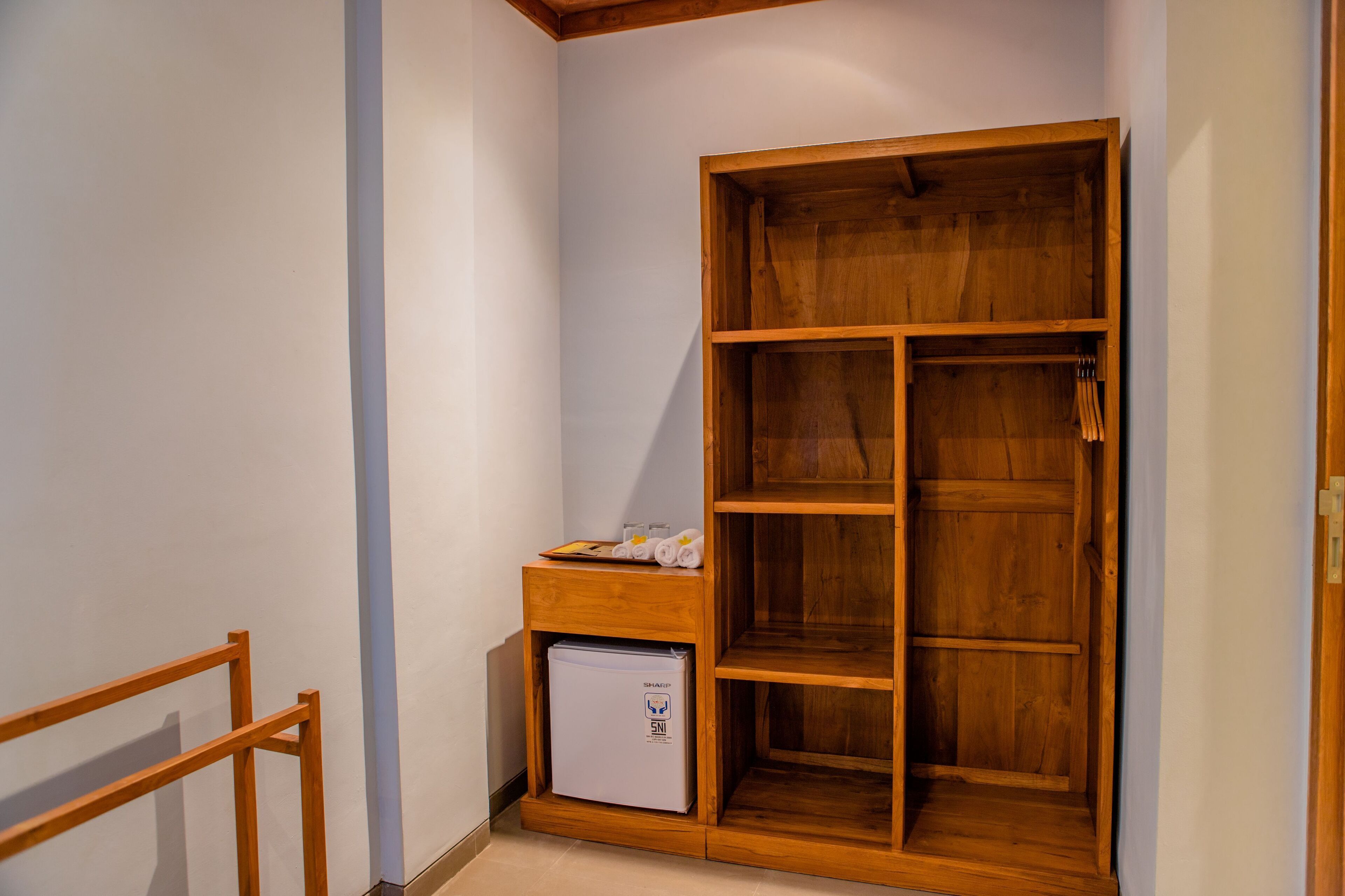 Habitación de esquina con armario de madera, un refrigerador pequeño y una banca de madera.