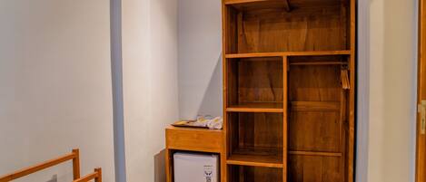 Habitación de esquina con armario de madera, un refrigerador pequeño y una banca de madera.