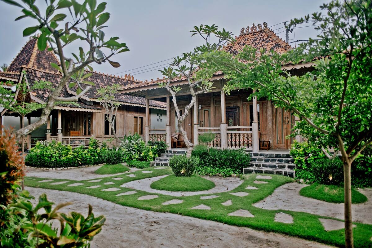 A traditional wooden house with a tiled roof, surrounded by a well-maintained garden with stone pathways and lush greenery.