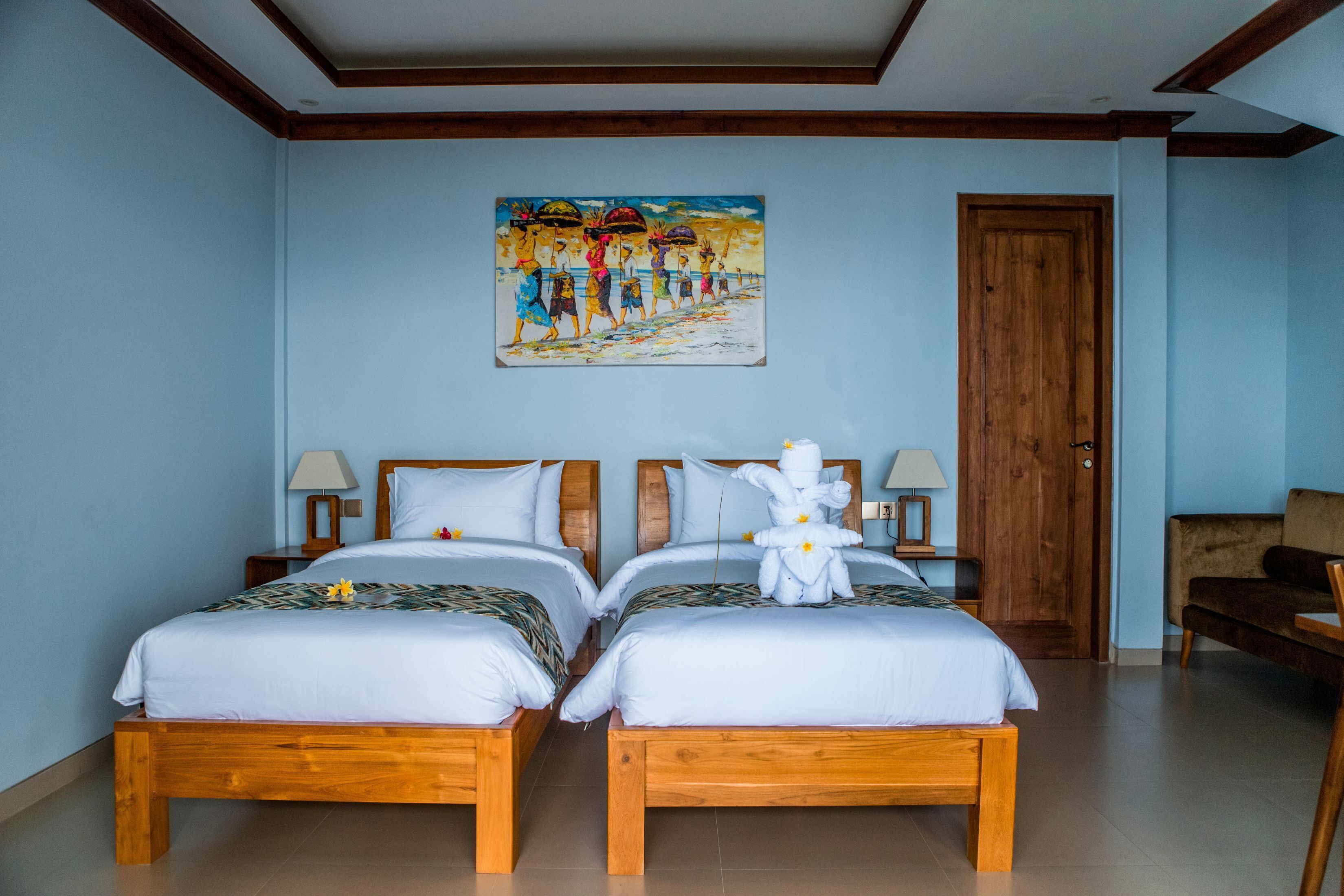 A hotel room with two wooden beds, a painting on the wall, a wooden door, and a chair.