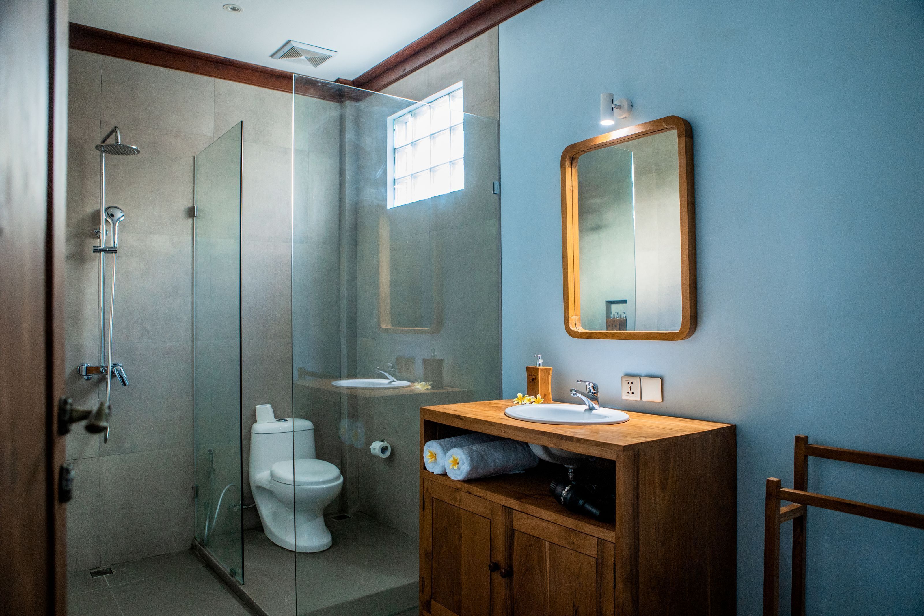 Un baño moderno con ducha envuelta en cristal, tocador de madera con espejo y un inodoro blanco.
