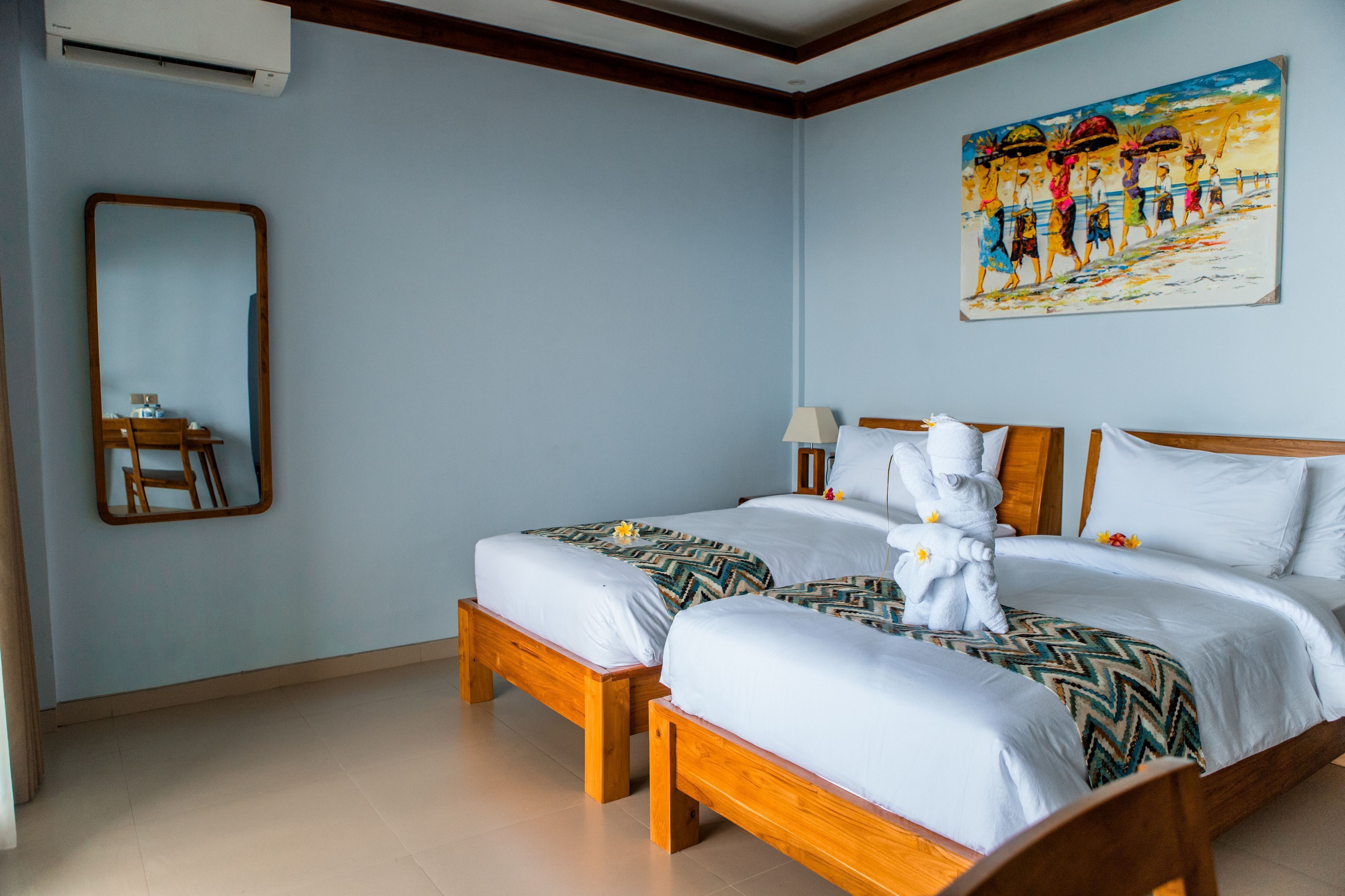 A hotel room with two wooden beds, a large mirror, a painting on the wall, and a wooden chair.