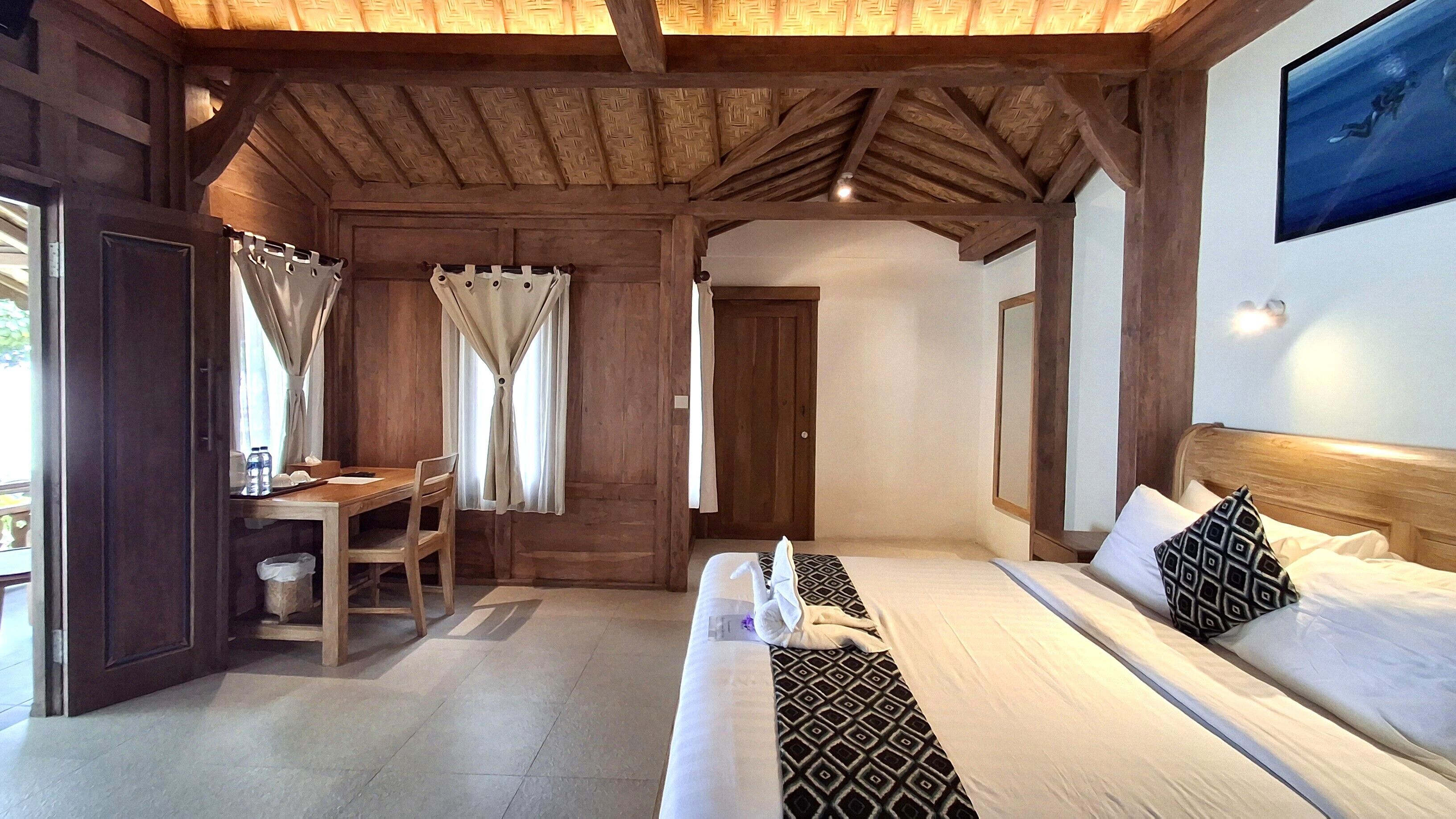 Een kamer met een houten plafond, een bed met beddengoed met een patroon, een bureau met een stoel en een raam met gordijnen.