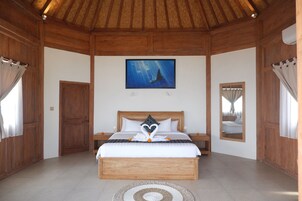 Une chambre aux murs lambrissés, avec un lit placé au centre, sous un tableau, et une porte, ainsi qu’un miroir.