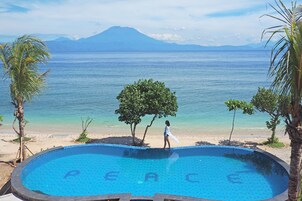 Una piscina con la palabra “PEACE” escrita en azulejos, rodeada de palmeras y vista a la playa.