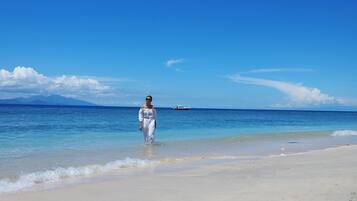 A person standing on a beach with clear blue water and distant mountains.