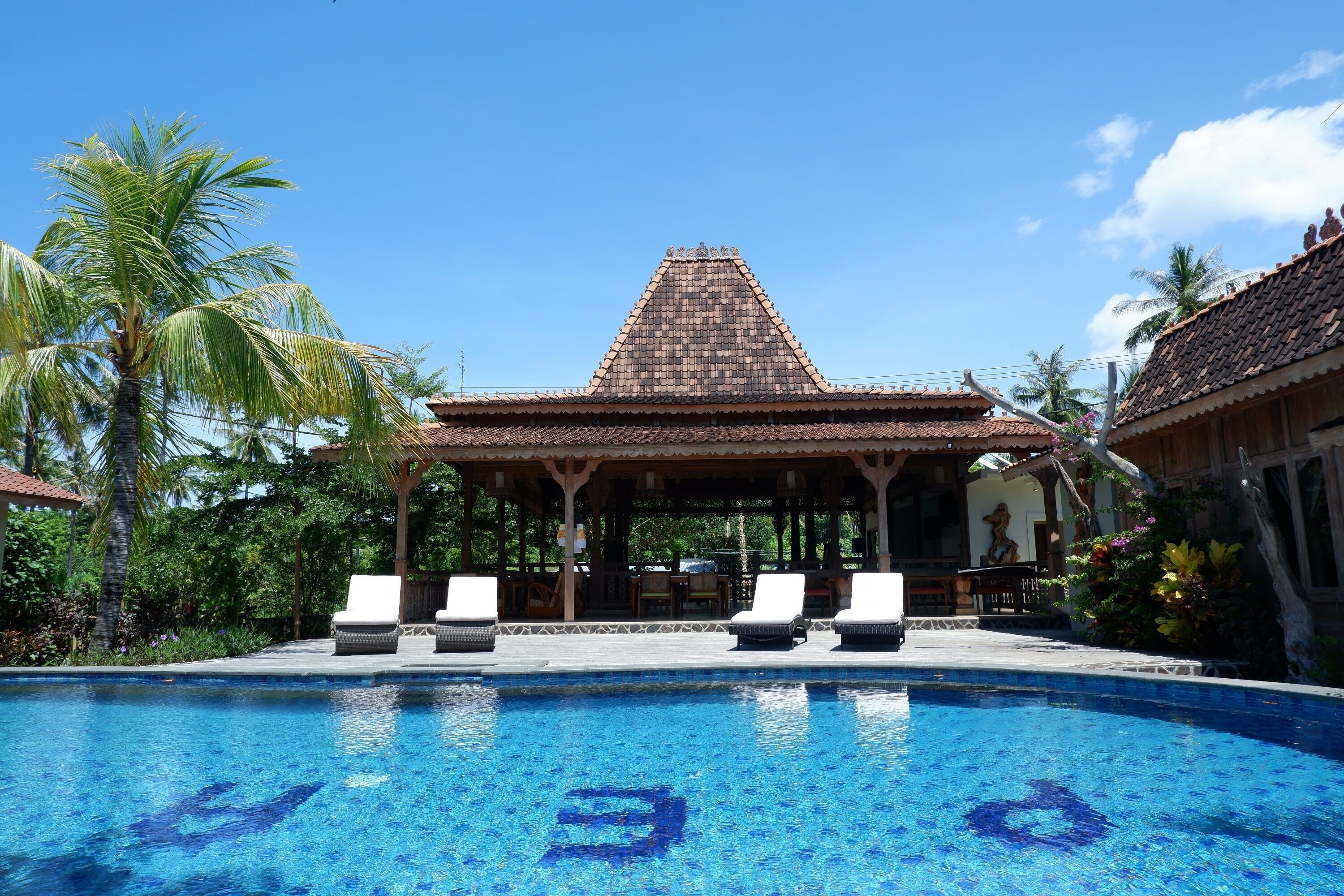A pool with lounge chairs, a gazebo, and palm trees.