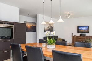A modern kitchen with a built-in oven, a dining table with chairs, and pendant lighting.