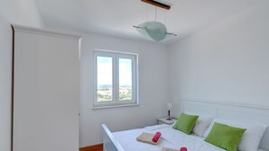 A bedroom with a bed, two pillows, a nightstand, a window, and a ceiling light fixture. - Superb Apartment in Murter with Hot Tub (Murter-Kornati)