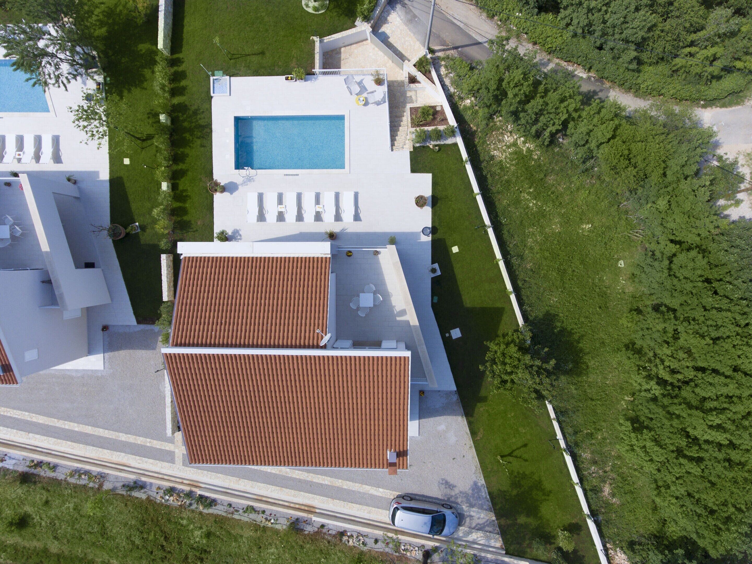 Vista aérea de un hotel moderno con piscina, mobiliario exterior y zona de estacionamiento.