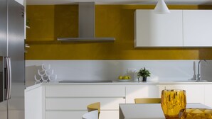 Una cocina moderna con armarios blancos, una pared de acento amarilla y un comedor con mesa y sillas amarillas.