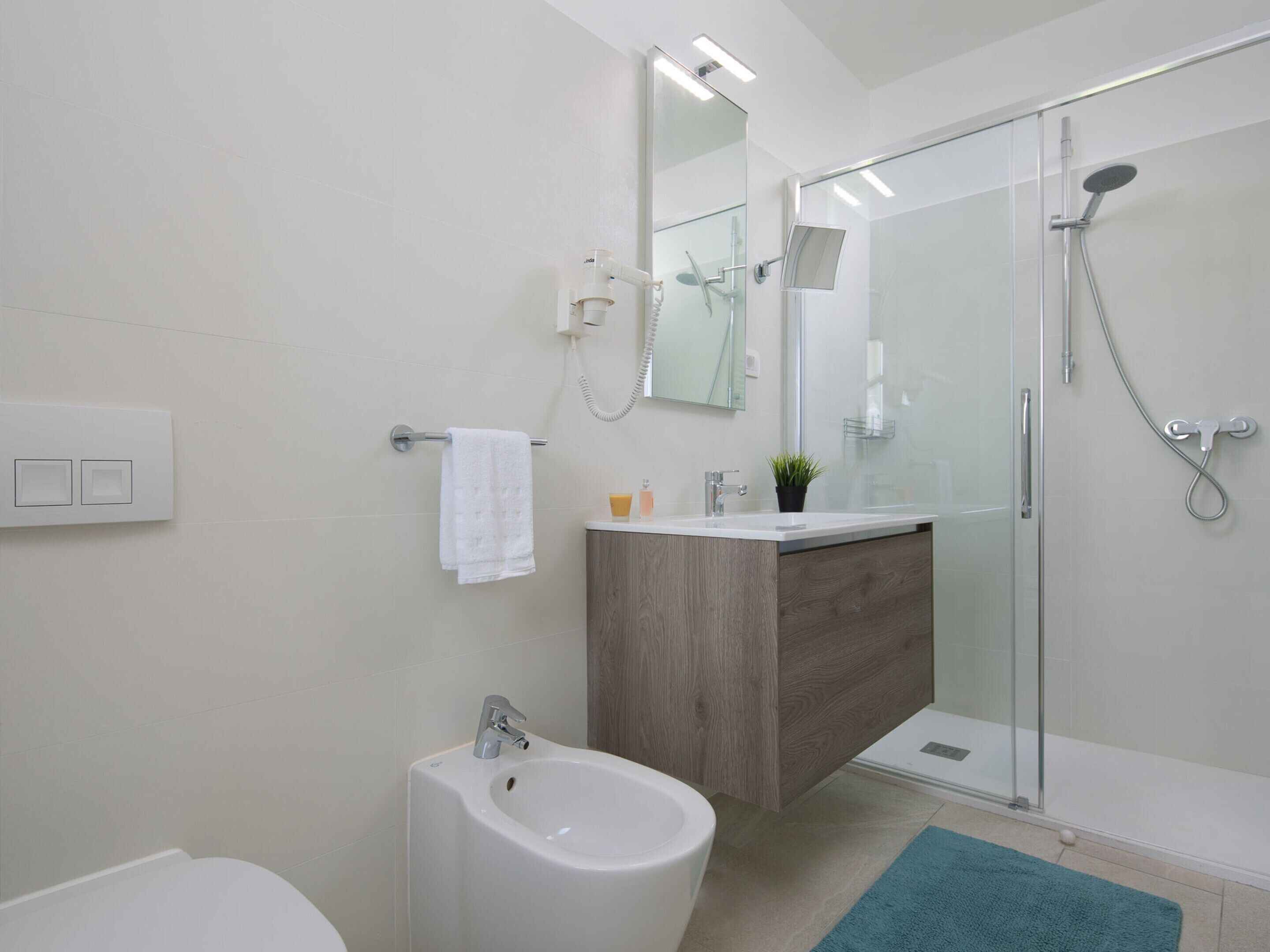 Ein modernes Badezimmer mit Duschkabine aus Glas, einem Bidet, einem Waschbecken mit Spiegel und einem Handtuch an einem Haken.
