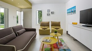 Una sala de estar moderna con un sofá, dos sillones, una mesita de centro, un televisor y un tapete colorido.