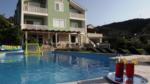 Ένα διώροφο κτίριο με πισίνα, ξαπλώστρες και μια περιοχή με μπαρ όπου σερβίρονται ποτά.