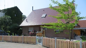 A brick house with a red-tiled roof, a wooden fence, and a tree in front. - Traditional Apartment near Sea in Kühlungsborn (Kuehlungsborn)