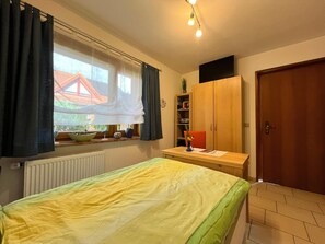 A bedroom with a bed, a window with curtains, a radiator, a wooden wardrobe, and a door. - Traditional Apartment near Sea in Kühlungsborn (Kuehlungsborn)