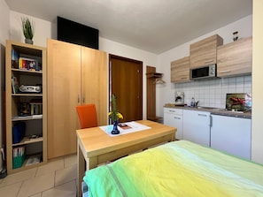 Una kitchenette compacta con microondas, cafetera y un pequeño comedor con mesa y silla.