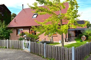 A brick house with a red tiled roof, a wooden fence, and a garden with potted plants. - Traditional Apartment near Sea in Kühlungsborn (Kuehlungsborn)