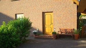 A brick building with a yellow door, a bench, and potted plants. - Traditional Apartment near Sea in Kühlungsborn (Kuehlungsborn)