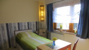 A bedroom with a bed, a table, and a chair. There is a window with curtains and a view of the outside. - Traditional Apartment near Sea in Kühlungsborn (Kuehlungsborn)