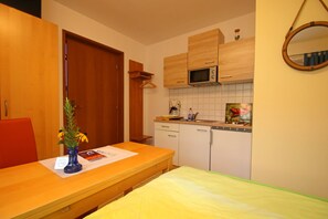 A compact kitchen with a microwave, sink, and cabinets. There's a dining table with a vase of flowers and a magazine.