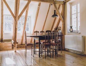 A room with a sloped ceiling, wooden beams, a table with chairs, a hanging light fixture, and a window with a view of trees. - Spacious Authentic Polish Farmhouse (Janowice Wielkie)
