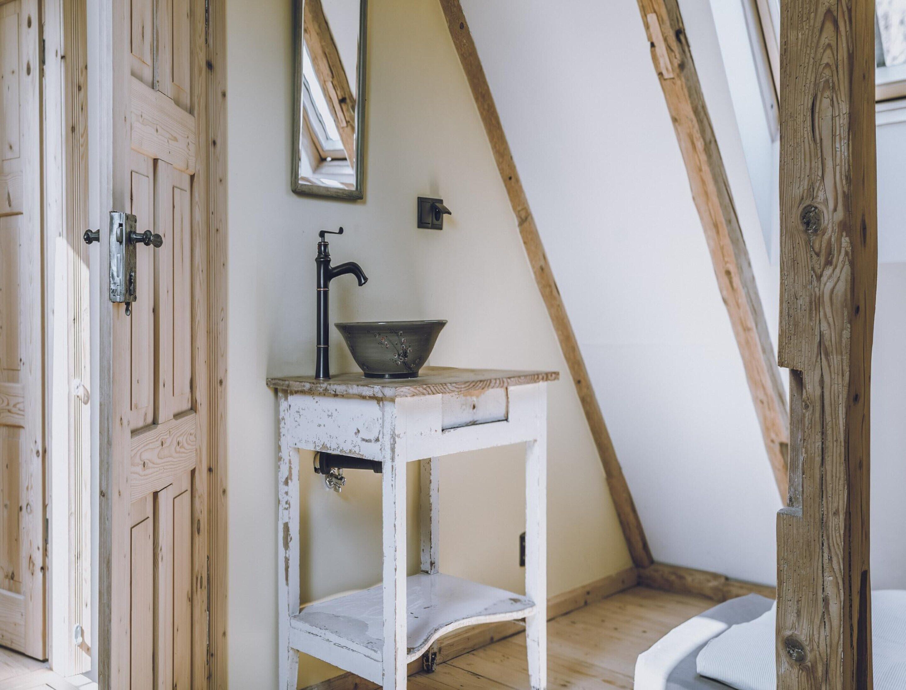 A rustic room with a white wooden door, a small white table with a black faucet, and a mirror on the wall.