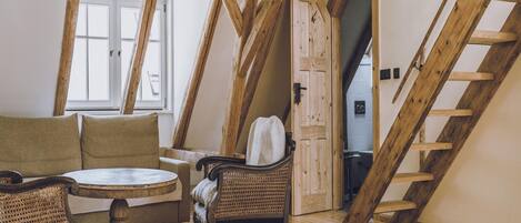 A loft bedroom with exposed wooden beams, a rattan chair, a round table, and a sofa.