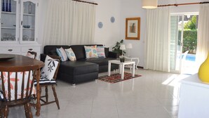 A living room with a dark sofa, a wooden dining table, and a white cabinet. - Villa Near Marina With Private Pool (Loulé)
