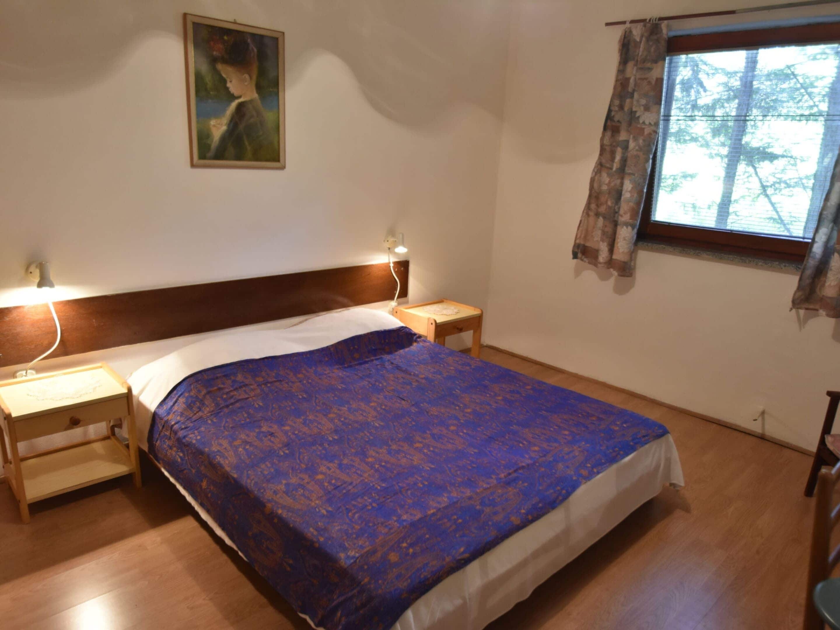 A bedroom with a bed, nightstands, a lamp, a painting on the wall, and a window with curtains.