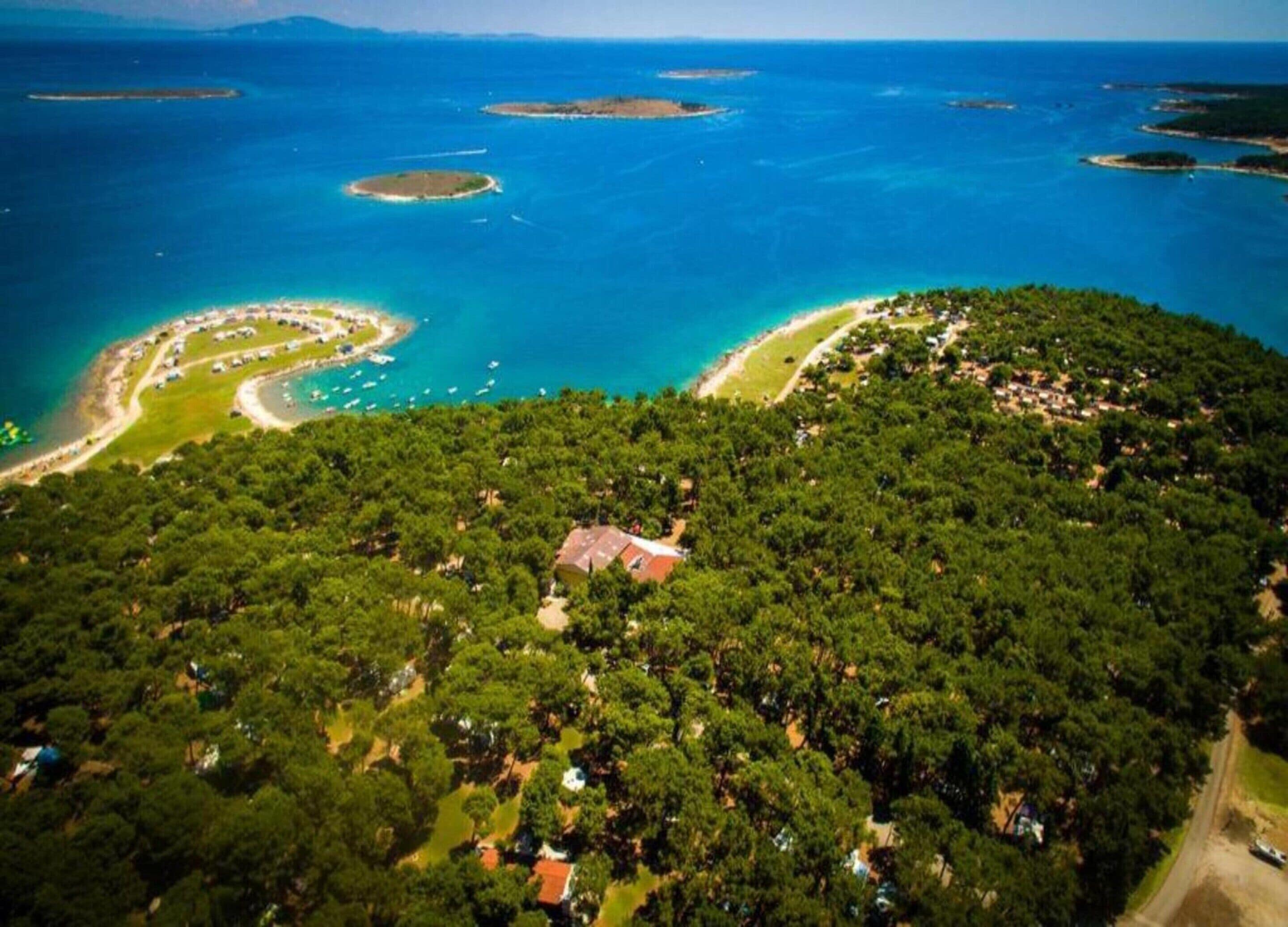 An aerial view of a coastal area with dense forest, a winding road, and a beach with boats.