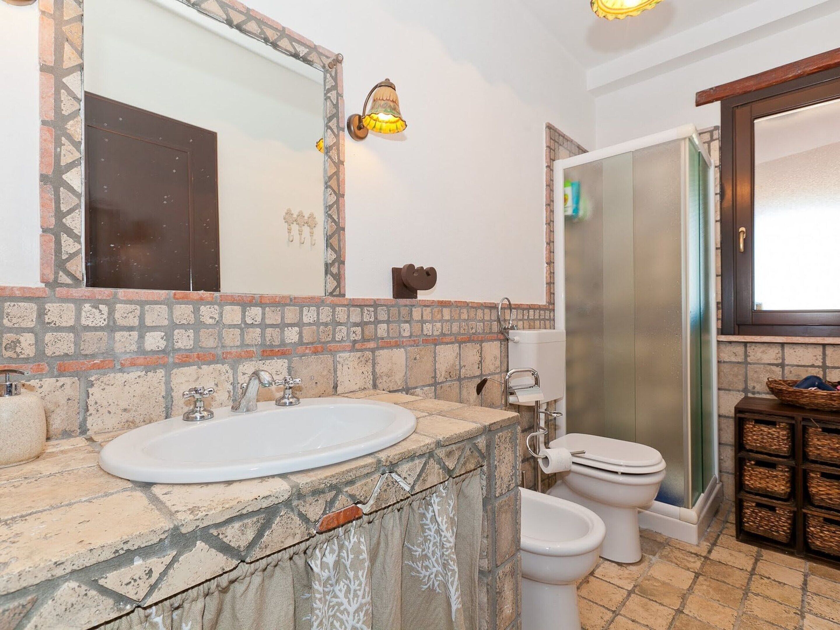Un baño con lavamanos de piedra, un espejo, inodoro y zona de ducha.