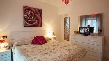 A bedroom with a large bed, a TV, a dresser, and a chandelier.