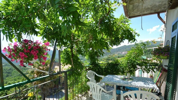 A terrace with a table and chairs, surrounded by greenery and a view of the countryside. - Belvilla by OYO Angie (Sesta Godano)