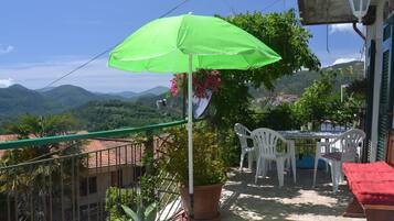 A balcony with a green umbrella, white chairs, a red cushioned bench, and potted plants.