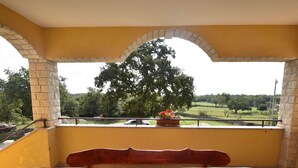 A balcony with a wooden table and bench, a potted plant, and a view of a tree and landscape. - Premium Apartment in Barban With Private Pool (Barban)