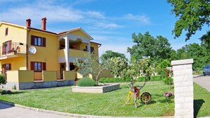 A yellow two-story building with a balcony, a satellite dish, and a bicycle in the garden. - Premium Apartment in Barban With Private Pool (Barban)