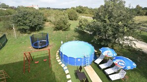 A backyard with a trampoline, a round pool, and a table with umbrellas. - Premium Apartment in Barban With Private Pool (Barban)