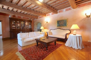 A living room with a wooden ceiling, a white sofa, a coffee table, and a red patterned rug.