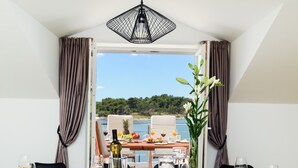 Une table à manger dressée pour six personnes, avec de l’argenterie blanche, des verres et des couverts, donnant sur un paysage pittoresque composé d’une étendue d’eau et de verdure.