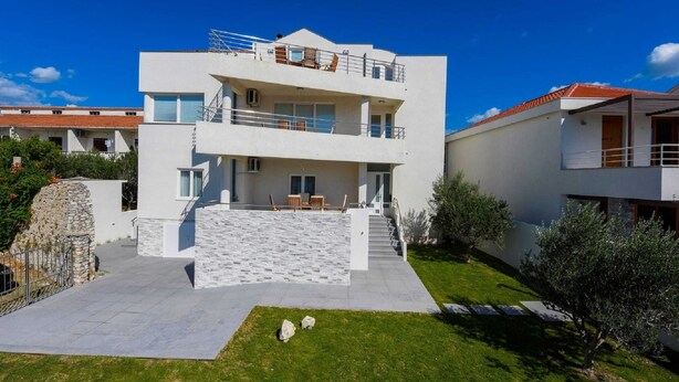 A modern two-story building with a flat roof, a stone retaining wall, and a paved courtyard with a small lawn area. - Modern Villa in Nin With Terrace (Nin)