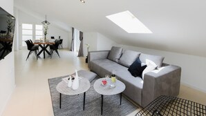 Un salon moderne avec un canapé gris, deux tables rondes et un coin repas comprenant une table et des chaises en bois.