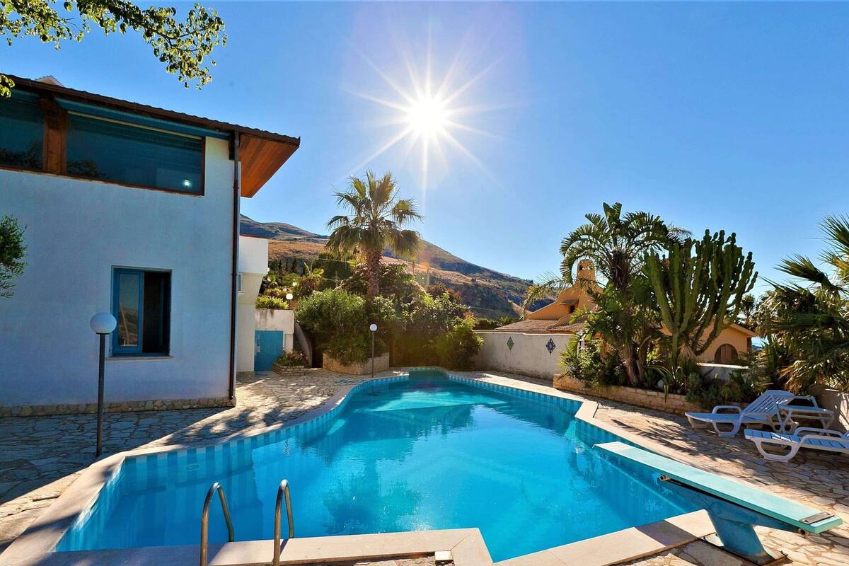Una piscina con bordo in pietra, circondata da palme e con una montagna sullo sfondo.
