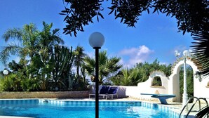 Une piscine à l’eau d’un bleu cristallin, entourée de palmiers et bordée d’un bâtiment blanc doté d’une entrée en arc de cercle.